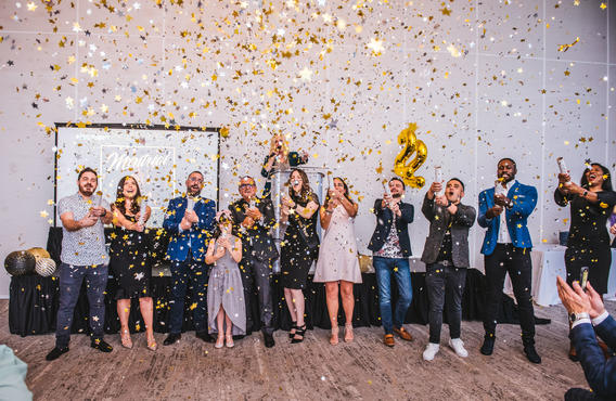 A group of 12 people celebrating by spaying confetti in the air.