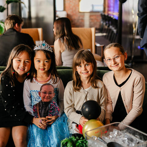 Four children smile together on a green couch surrounded by balloons and festive décor during the gala evening.