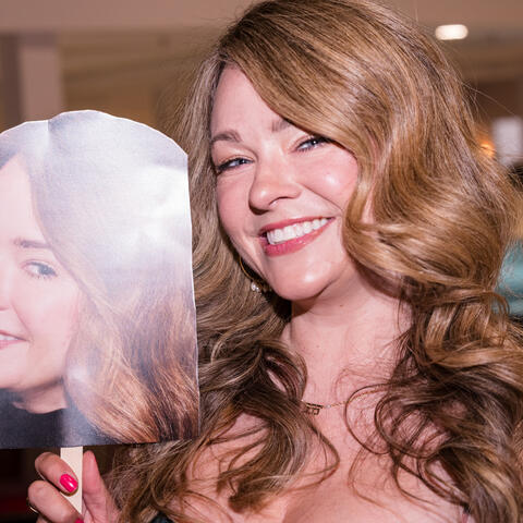 A participant holds a large face sign while posing for a playful portrait during the event reception at the venue.