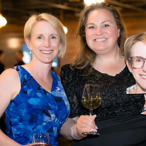 Two participants pose while one attendee holds a playful face sign during the reception.