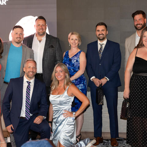 A group of participants poses together on stage in formal attire during the Visionaries of the Year celebration.