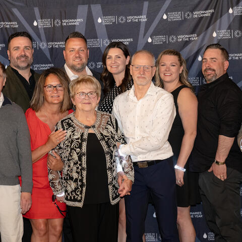 A large group of participants gathers in front of the Visionaries of the Year backdrop for a posed event photo.