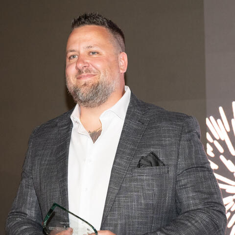 An award recipient stands on stage holding a glass trophy during the Visionaries of the Year celebration.