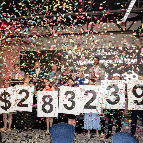 Participants on stage celebrate under falling confetti while holding fundraising totals at the Visionaries event.