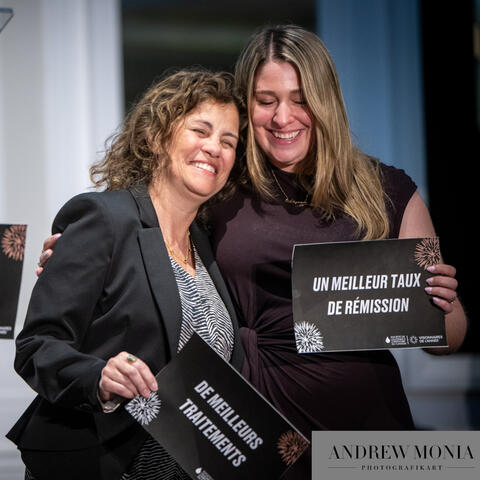 Participants on stage smile and hold signs highlighting achievements while standing close together during a celebratory moment at the event.