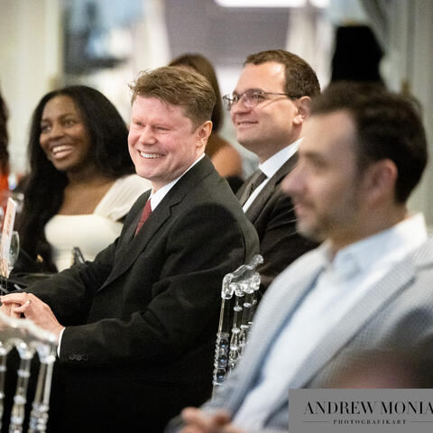 Participants seated at banquet tables share a light moment, smiling and turning toward conversation during an elegant evening fundraising event.