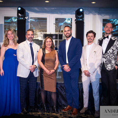 Participants gather on stage in formal attire, standing side by side as they are recognized together during a fundraising event.