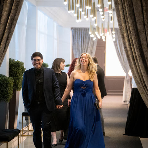 Participants arrive at a gala, walking beneath black and gold balloons and warm hanging lights in a welcoming entrance.