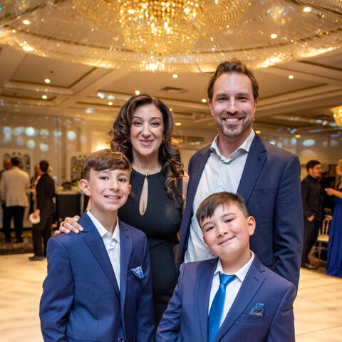 Participants pose together under a sparkling chandelier at a formal event, dressed elegantly and gathered closely on the ballroom floor.