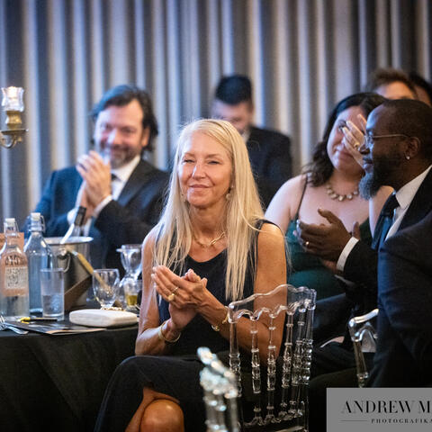 Participants seated at a decorated table applaud together, surrounded by candlelight and glassware during a warm and engaging fundraising event.