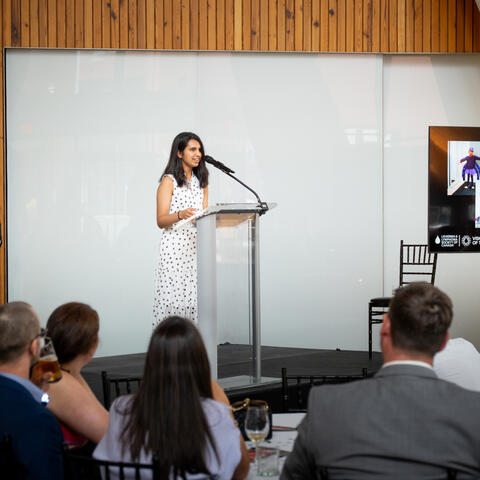 Participants stand together on stage listening as a speaker addresses attendees during the formal program segment.
