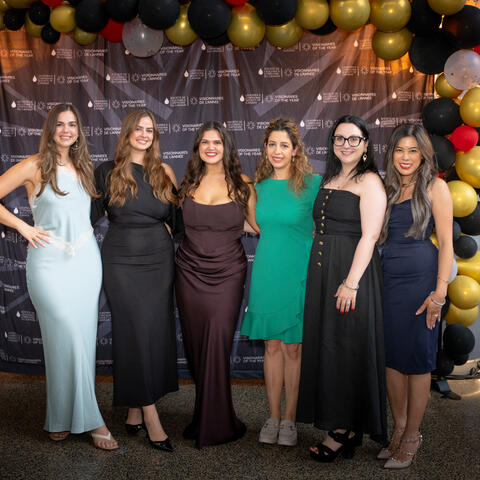 Participants pose together in front of a branded backdrop and balloon display during a celebratory photo moment.